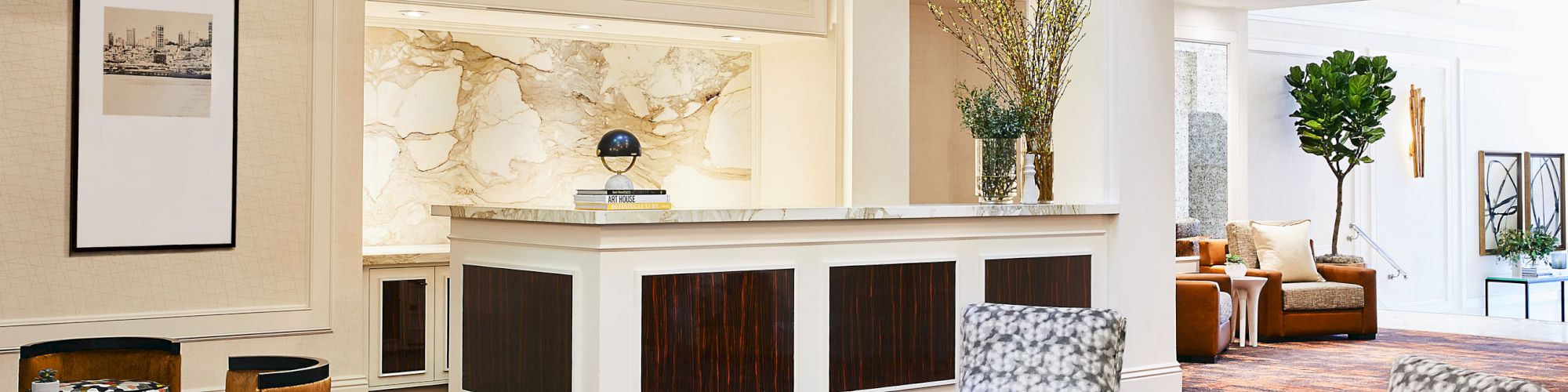 A modern, well-lit lobby with stylish furniture, a reception desk, plants, and a seating area adorned with books and decor items.