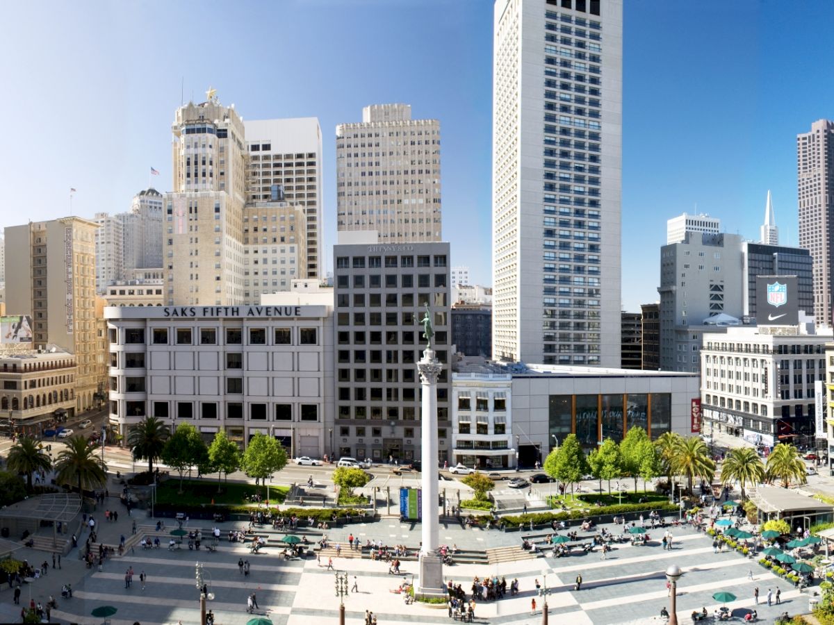 The image shows a cityscape with high-rise buildings surrounding a public square featuring a central monument and green spaces where people gather.