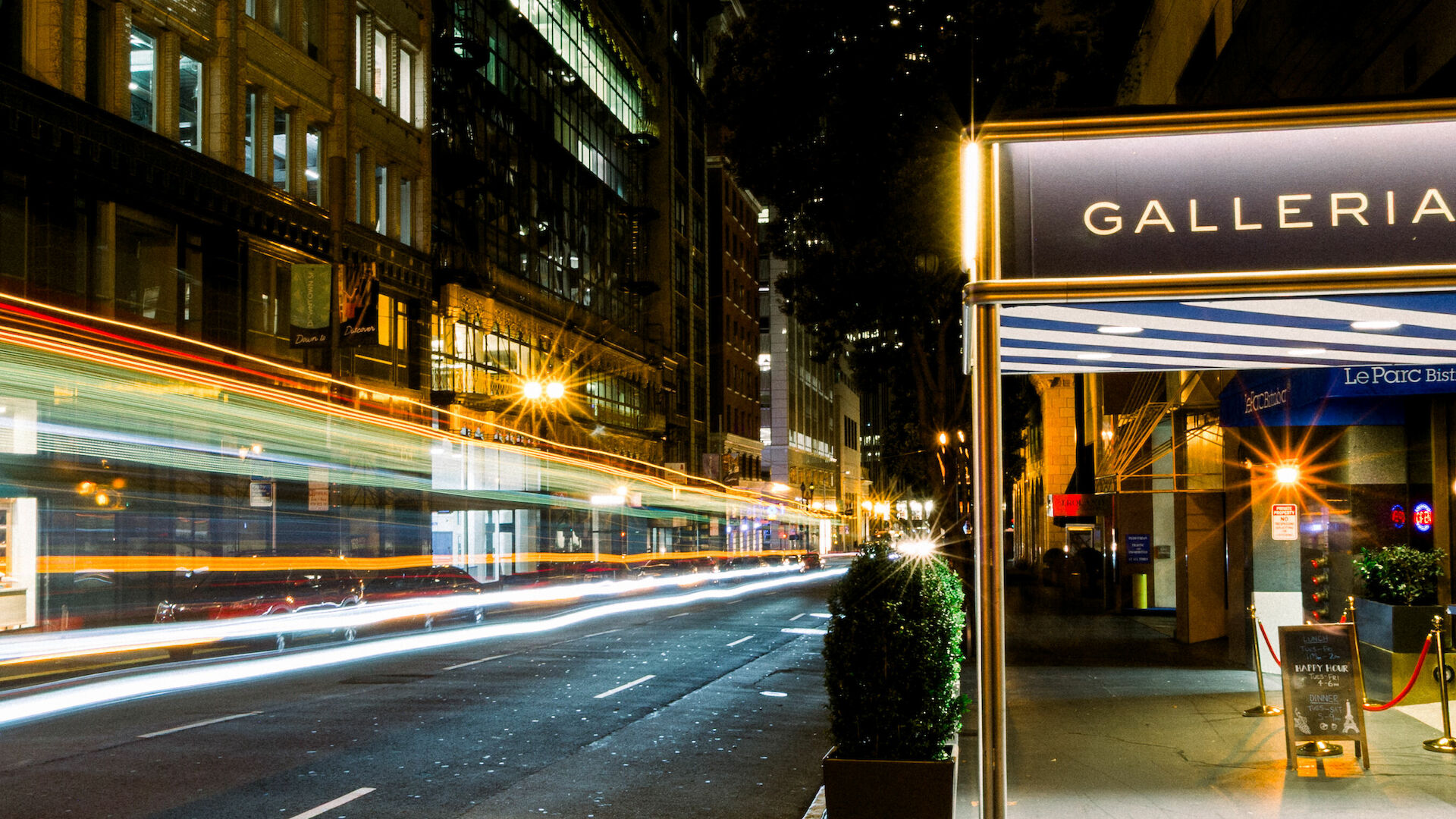 Night street scene with light trails from moving vehicles and a view of the Galleria Park Hotel entrance, with some streetlights glowing.