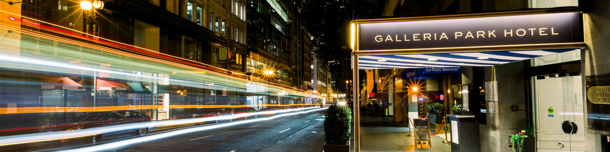 Night street scene with light trails from moving vehicles and a view of the Galleria Park Hotel entrance, with some streetlights glowing.