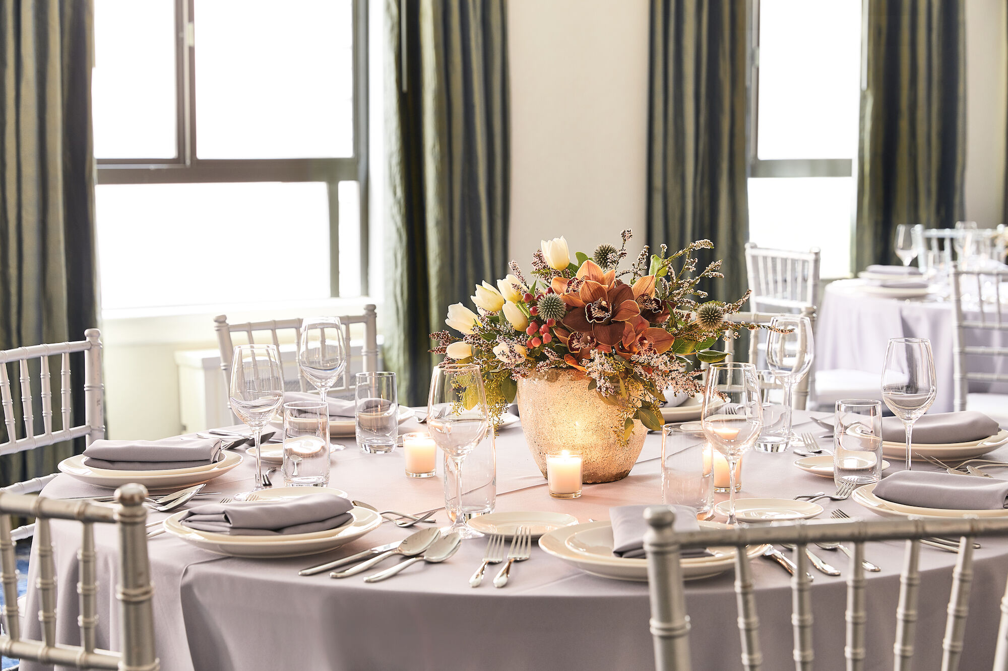 A beautifully set banquet table with glassware, candles, and a bouquet centerpiece in a gold vase.