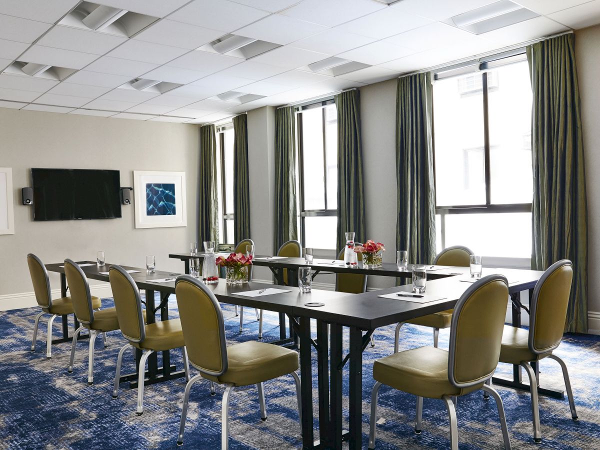 The image shows a modern conference room with a U-shaped table setup, green chairs, large windows, and floral centerpieces on the tables.