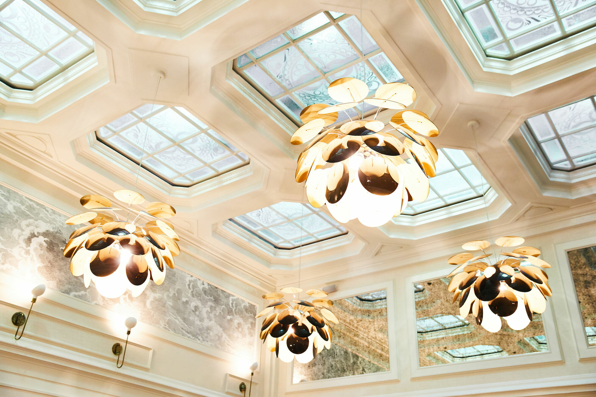 The image shows an elegant ceiling with several ornamental light fixtures and decorative glass panels, creating a sophisticated atmosphere.