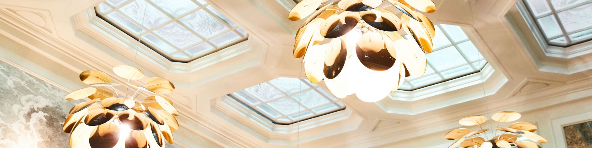 The image shows an elegant ceiling with several ornamental light fixtures and decorative glass panels, creating a sophisticated atmosphere.