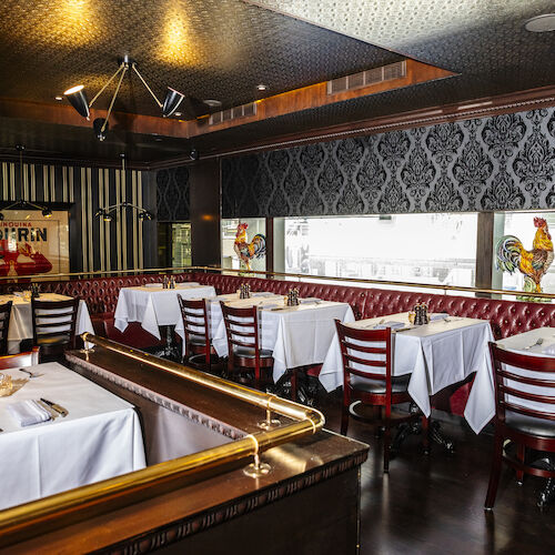 A restaurant interior with red leather booths, wooden chairs, white tablecloths, and rooster art on the windows.