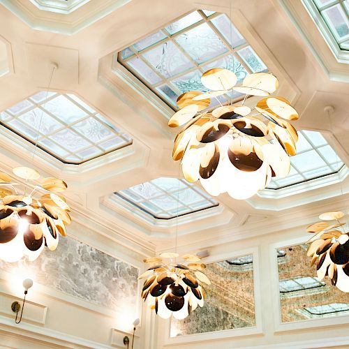 The image shows a ceiling with multiple decorative light fixtures and large, decorative skylights, adding elegance to the interior space.