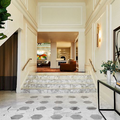 A modern hallway with marble floors and stairs; decor includes plants, abstract artwork, and a console with books and vases leading to a seating area.