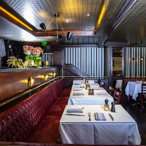 A cozy restaurant interior with red leather seating, white tablecloths, striped walls, and decorative lighting.