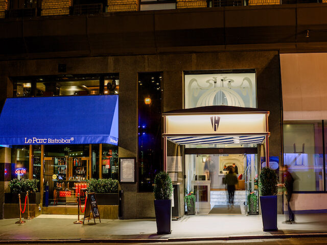A nighttime view of a hotel exterior with a blue awning and lit entrance.