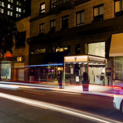 Street view at night with light trails from cars, showing the entrance to Galleria Park Hotel, surrounded by buildings and trees.