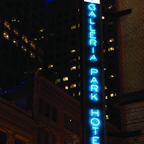 A neon sign for "Galleria Park Hotel" glows against a backdrop of tall, lit-up buildings at night.