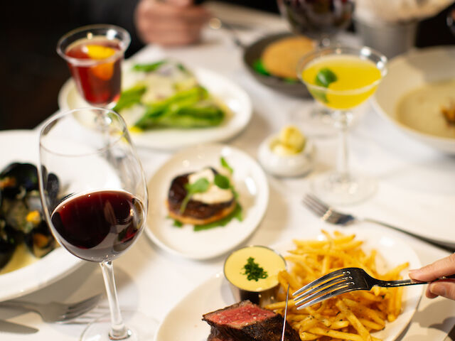 A dinner table set with various dishes, glasses of wine and juice, and a hand holding a fork and knife.