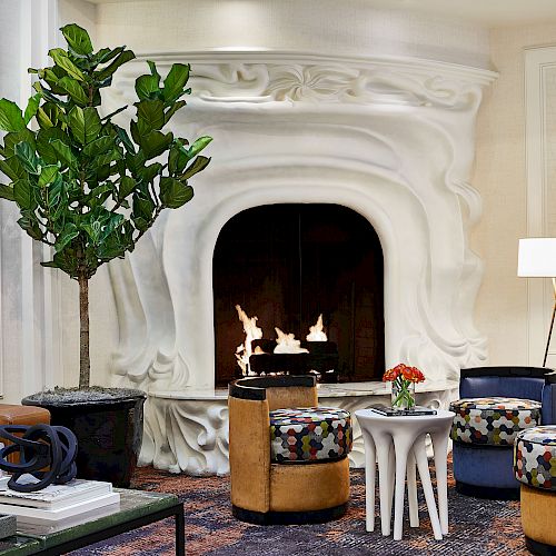 A cozy, modern living room featuring a unique white fireplace, seating, a large plant, and art on the walls for a stylish yet comfortable setting.