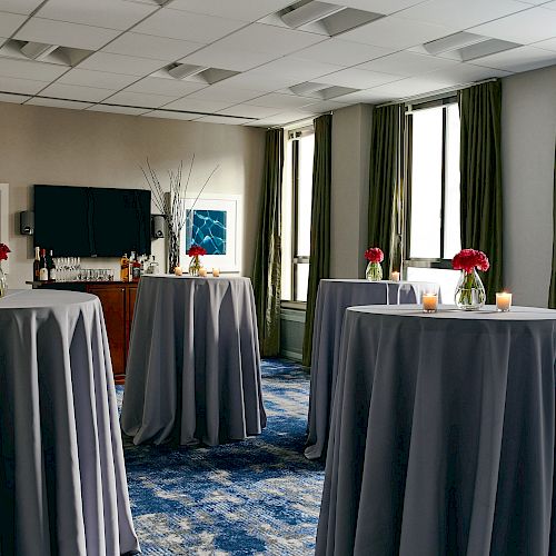 A room set up for an event with tall cocktail tables draped in gray cloth, each adorned with flowers and candles.