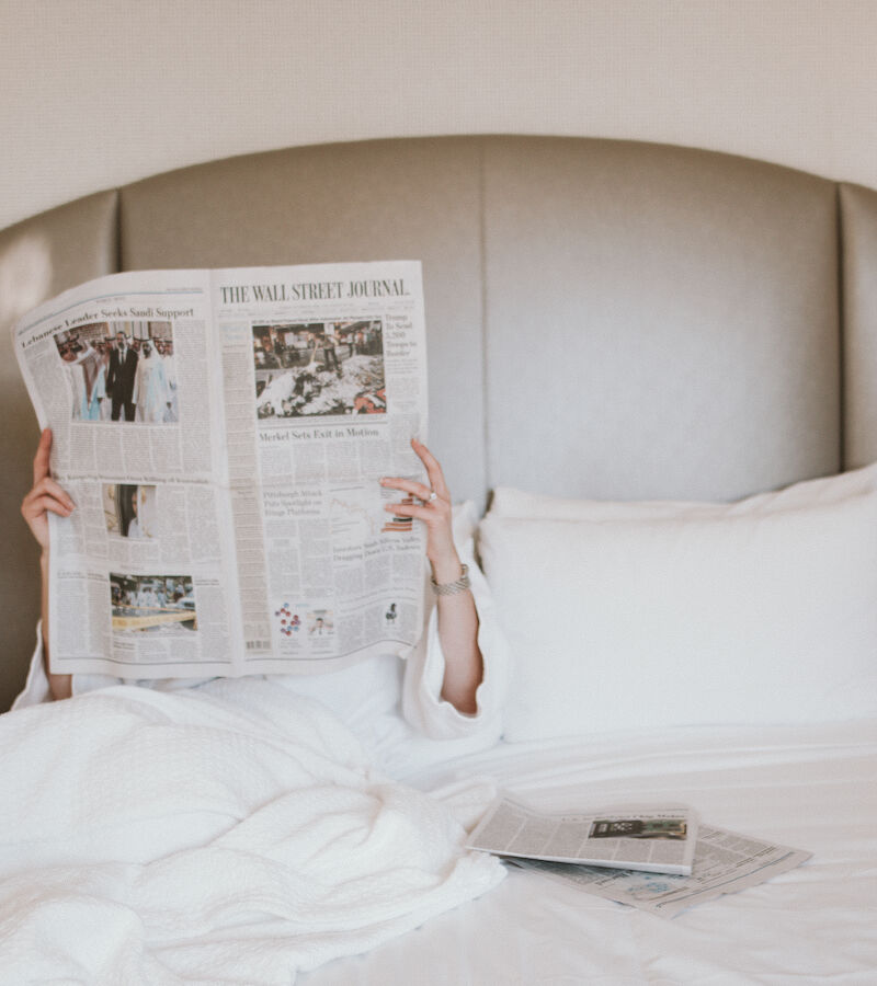 A person in a white robe lying in bed reading The Wall Street Journal