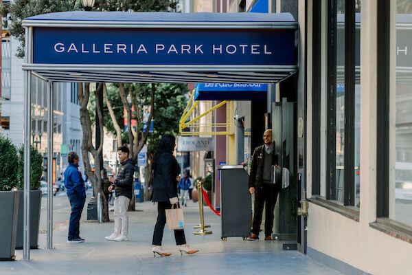 A hotel entrance with a blue awning and people walking in and out.