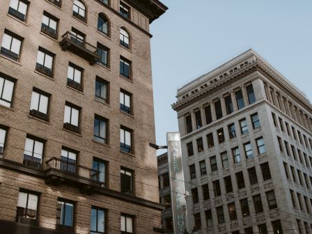 Two multi-story buildings with numerous windows against a clear sky. A vertical sign is partially visible between them.