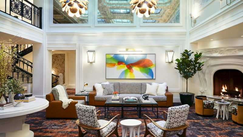 A spacious lobby with a high ceiling, a large fireplace, a staircase, and a seating area with a sofa, armchairs, and a coffee table.