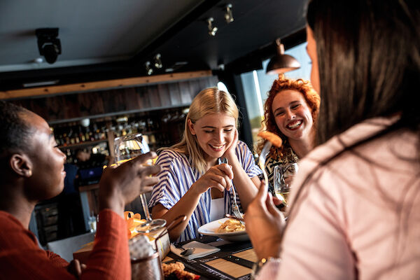 A group of people are sitting at a restaurant table, laughing and enjoying a meal together.