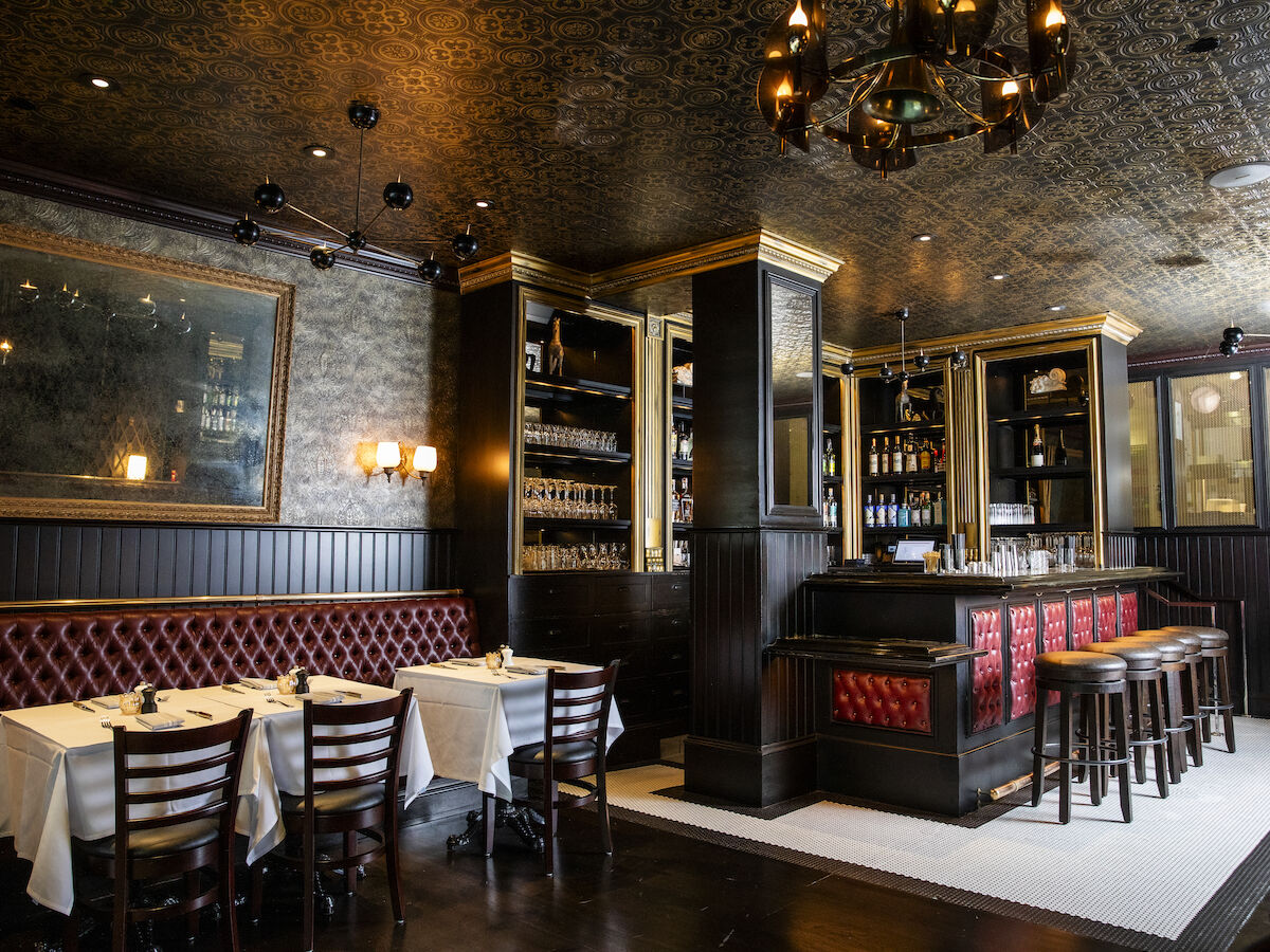 The image shows an elegant restaurant interior with a bar, red cushioned seating, tables set with white cloths, and ornate lighting fixtures.