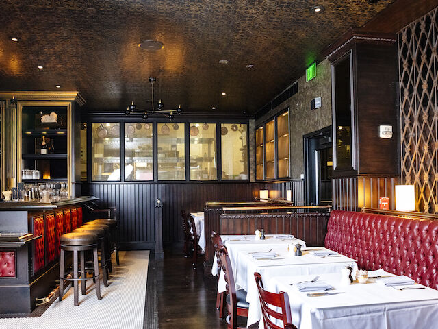 A restaurant dining area with a bar, booths, and tables set for meals.