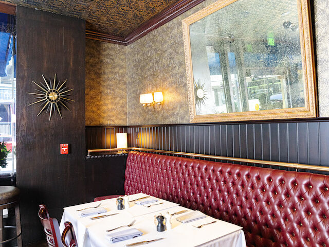 A dining area with a red leather booth, a table set for dinner, and a large mirror on the wall.