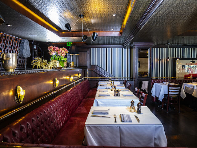 A restaurant dining area with white tablecloths, red leather booths, and gold accents.