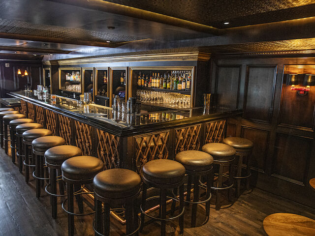 a dimly lit bar with stools and shelves of bottles