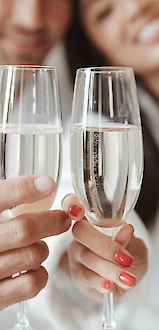 Two people wearing white robes clinking champagne glasses, smiling and enjoying a moment together.