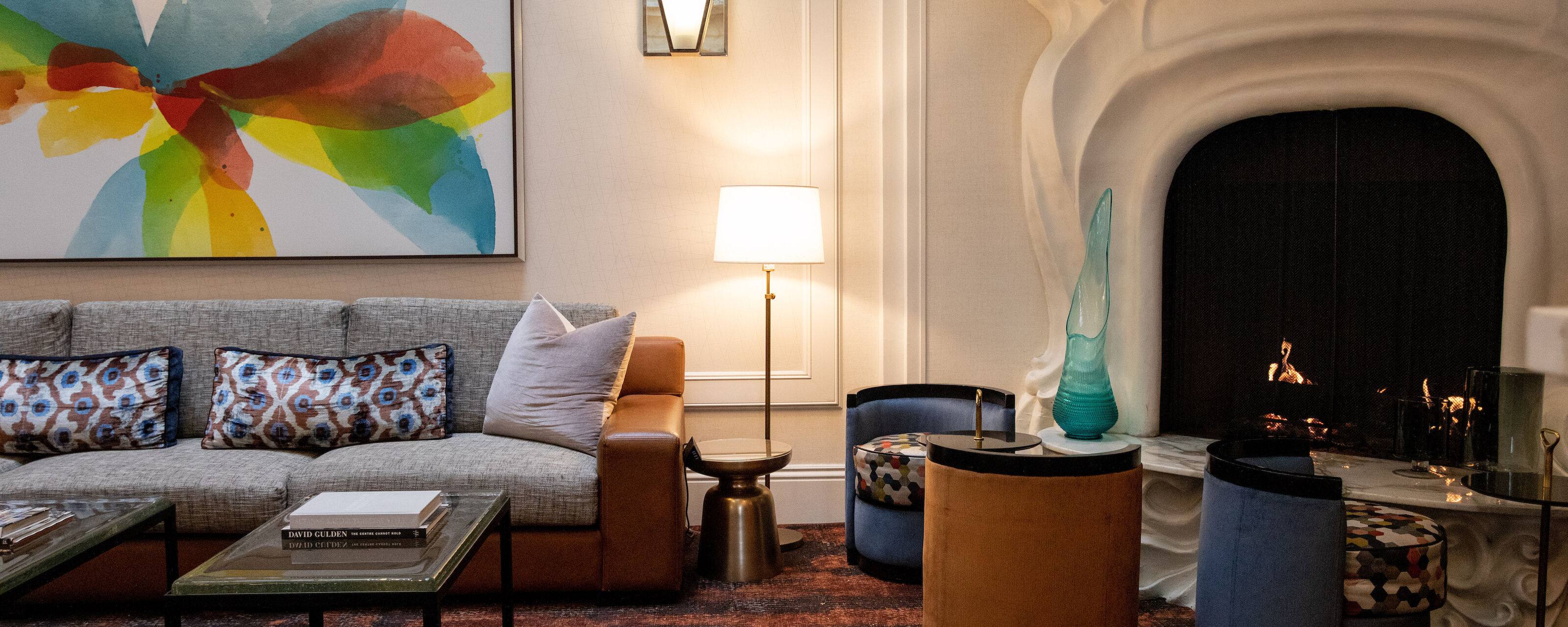 A stylish lobby with a gray sofa, coffee tables, chairs, and a lit fireplace.