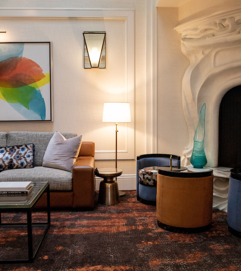 A lobby with a sofa, chairs, coffee table, lamp, and fireplace.