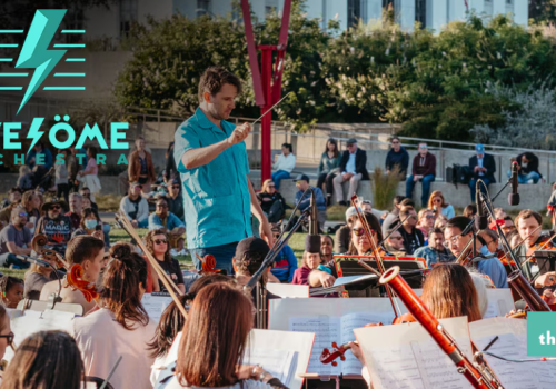 A conductor leads the Awesome Orchestra in an outdoor concert at Thrive City, surrounded by a large audience in a lively setting.