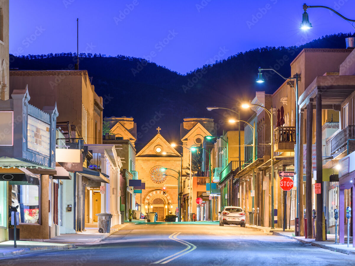 A street in what appears to be a quaint town, with shops on either side and a church at the end, set against hills and a twilight sky.