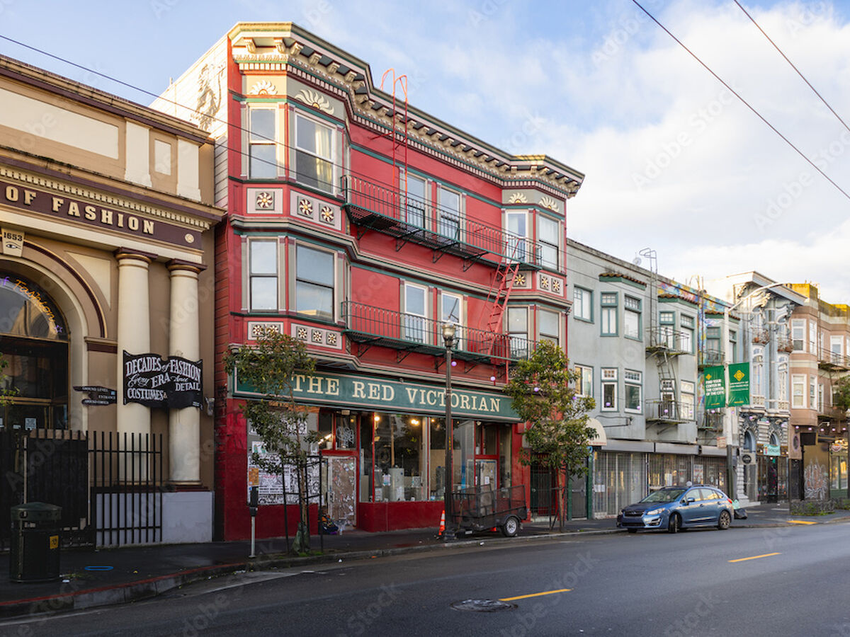 Street with colorful buildings, including "The Red Victorian," cars parked on the side, and a clear sky above.