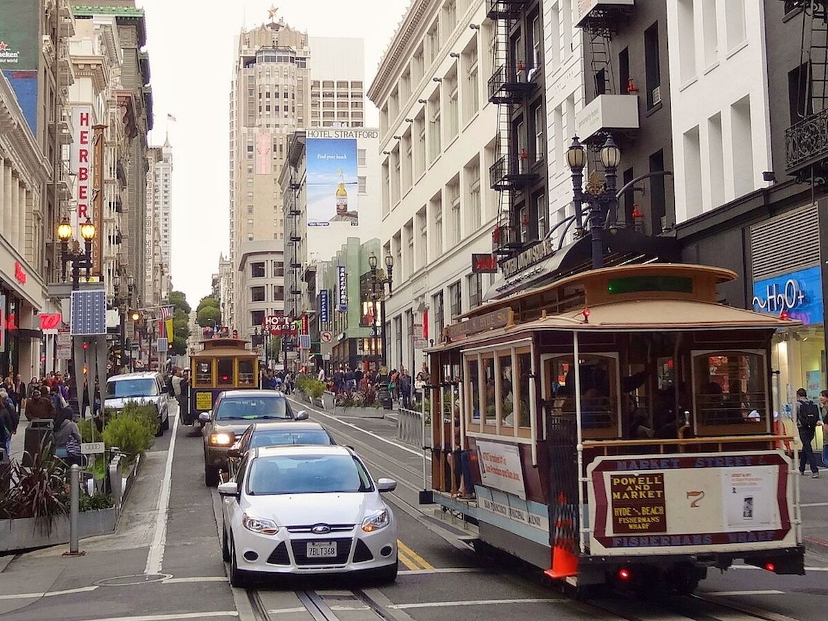 A bustling city street with cable cars, cars, and pedestrians under tall buildings.