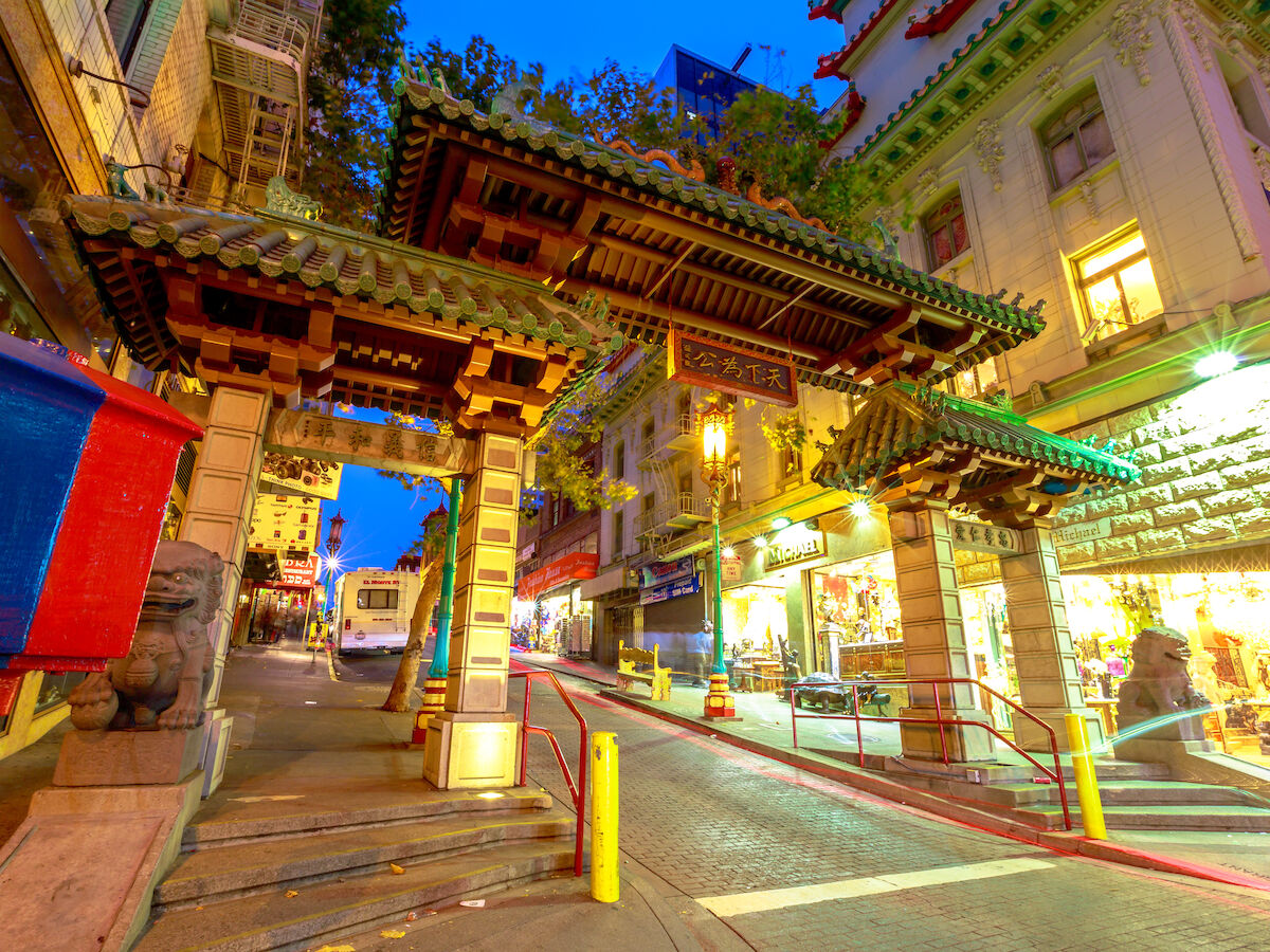 Decorative archway at Chinatown entrance on a vibrant street, adorned with lights and surrounded by shops in an urban setting.