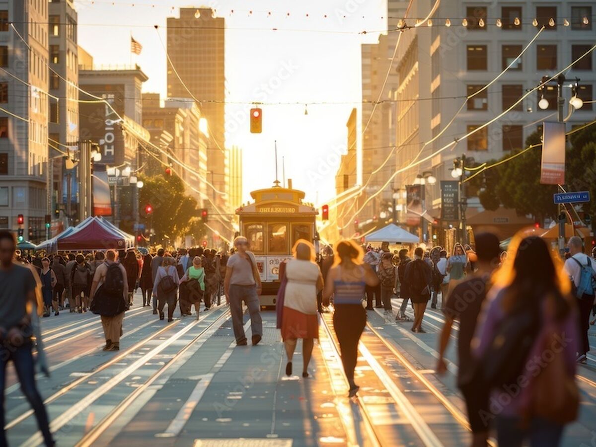 The image shows a busy city street with many people walking and a tram in the center, set against a sunset backdrop.