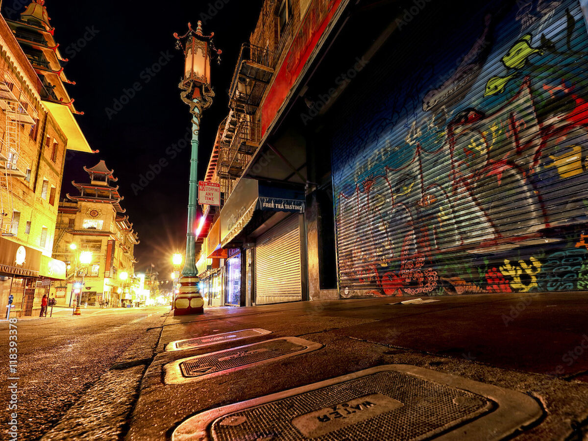 A nighttime street scene with vibrant graffiti on a shuttered storefront, illuminated by street lamps, with distinctive architecture.