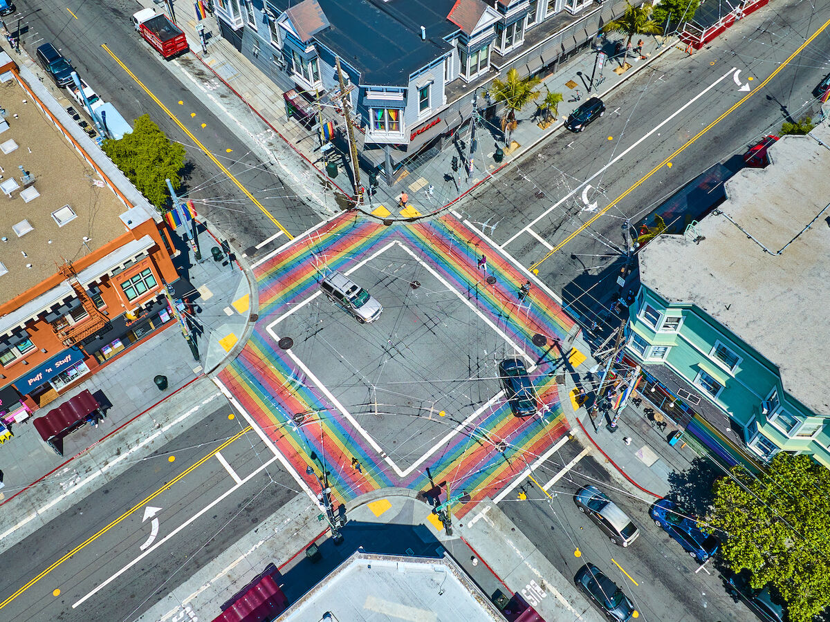 Aerial view of a city intersection with rainbow crosswalks surrounded by colorful buildings and streets.