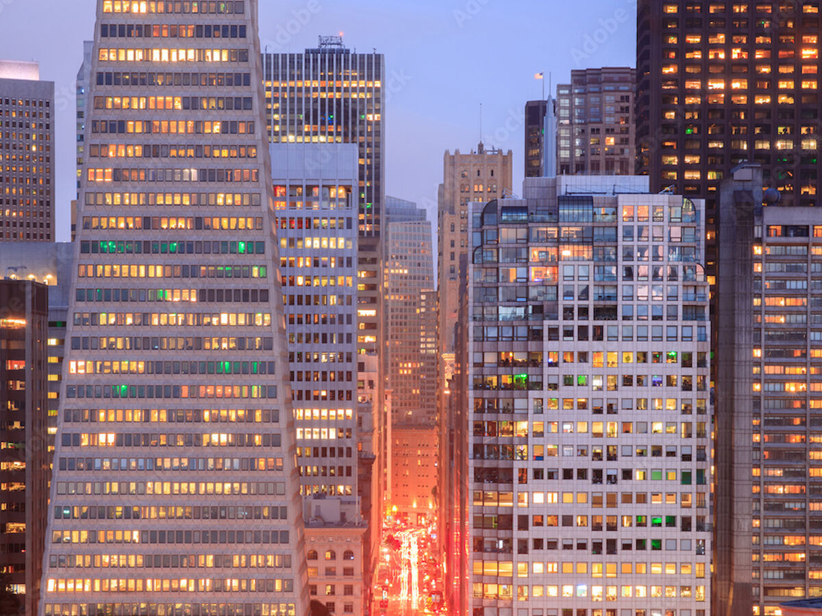 Skyscrapers in a city skyline during dusk, with buildings illuminated and a busy street visible below.