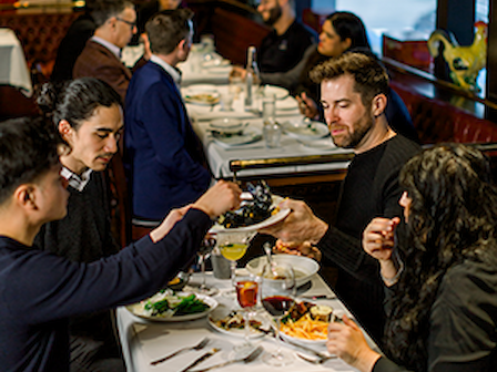 A group of people sitting at a restaurant table, enjoying a meal together with drinks, engaging in conversation.