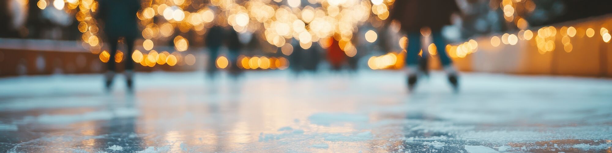 People skating on an ice rink with warm string lights sparkling in the background at night, creating a festive glow.