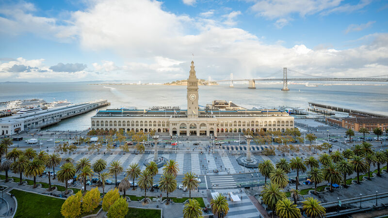Aerial view of a large public building with a clock tower, surrounded by a plaza and waterfront area.