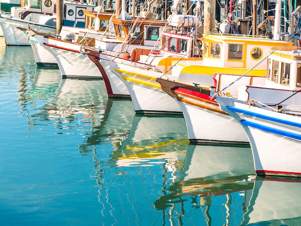 Colorful boats docked along a calm harbor, their reflections shimmering in turquoise water, a sunny seaside scene.