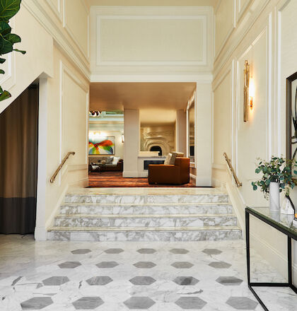 A bright, traditional-style foyer with a checkered floor, arched doorway, decorative niches, and a long hallway leading to a living area.