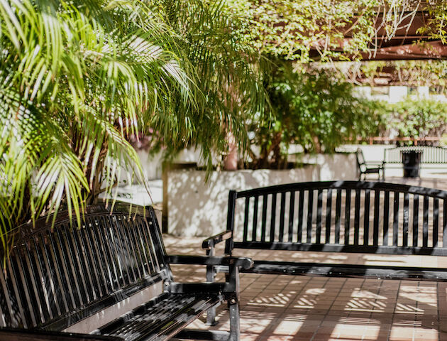A small outdoor patio with a metal table and chairs beside a stone wall, potted plants, and a shaded, tranquil garden scene.