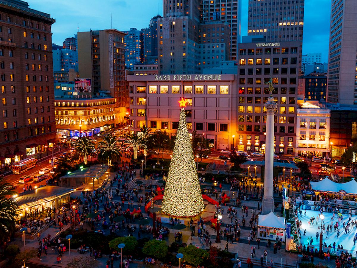 This image shows a festive city square with a large, illuminated Christmas tree, surrounded by people, holiday lights, and an ice skating rink.